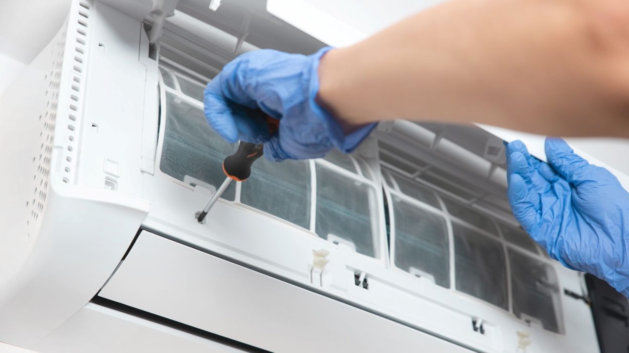 AC repair in Smyrna, GA: Technician in blue gloves repairs an air conditioner. AC maintenance ensures efficient cooling in Atlanta, GA.