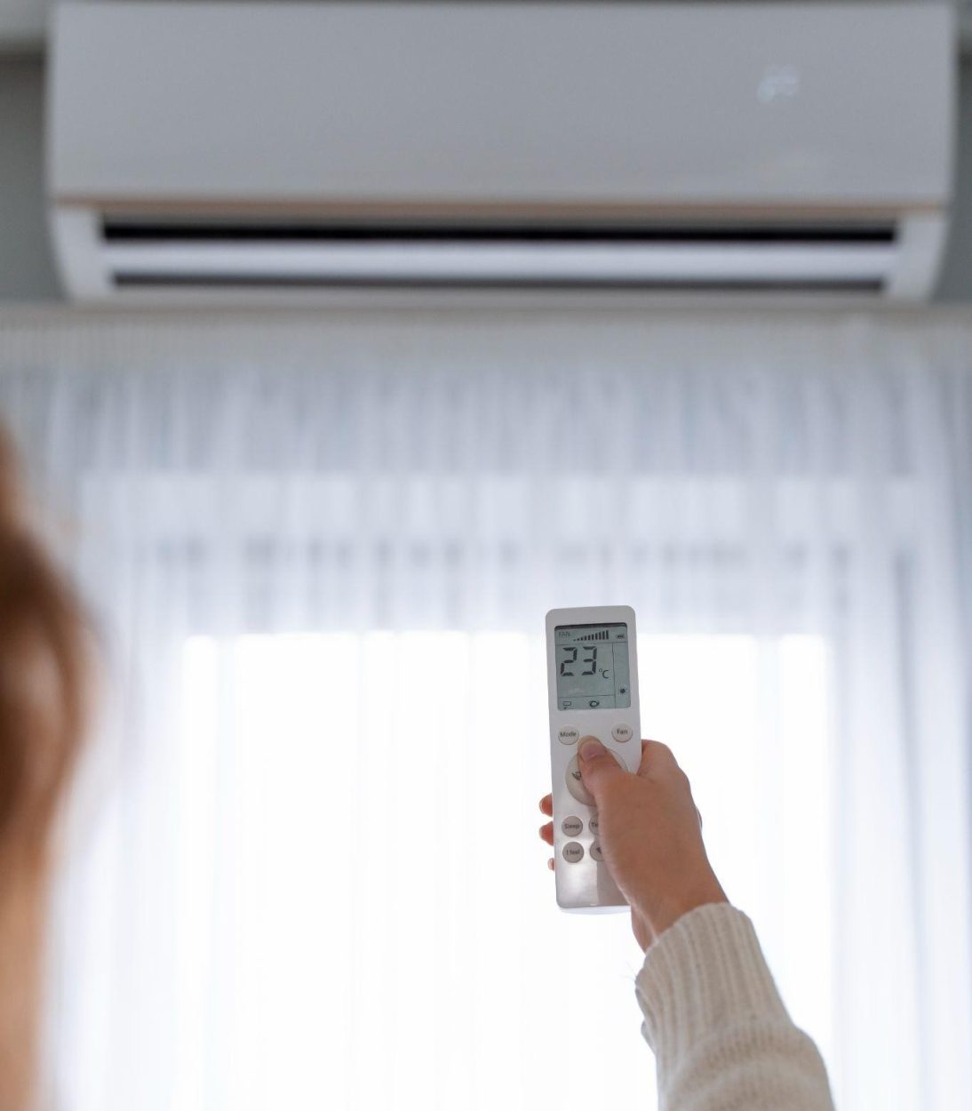 Person adjusting AC with remote. Choosing the right AC for Atlanta Homes involves considering factors like energy efficiency and cooling capacity.