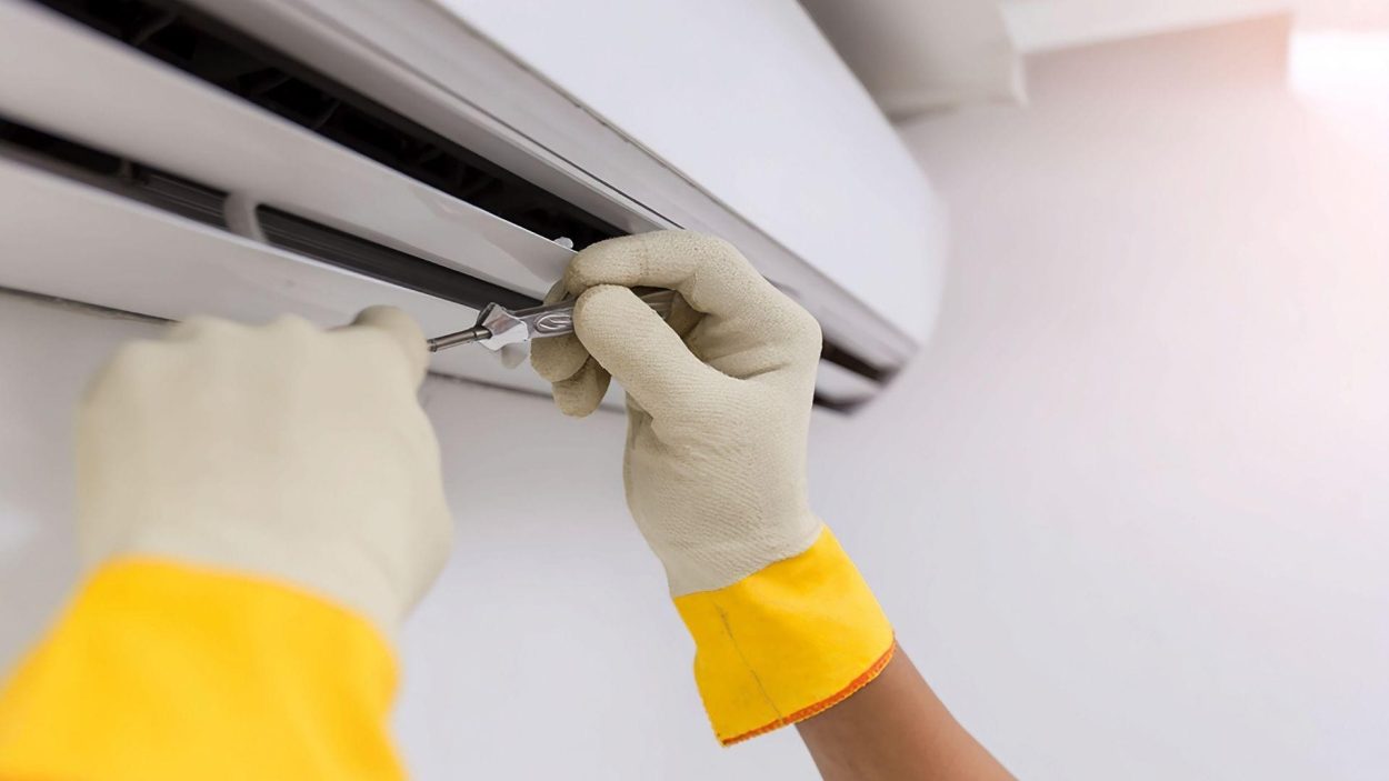 Air conditioner repair in Atlanta, GA. Technician's hands in gloves fixing an AC unit with a screwdriver. Choosing the right AC factors.