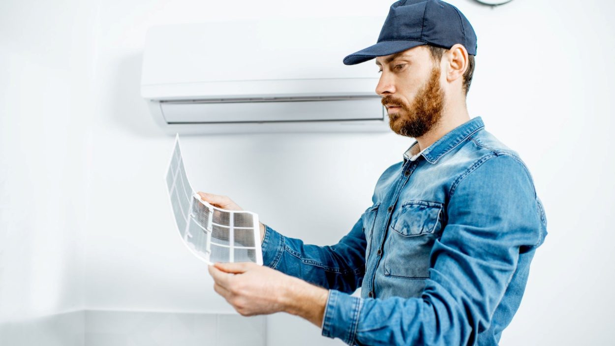 Air Conditioner Maintenance in Atlanta, GA: Technician inspecting a dirty AC filter under a wall-mounted air conditioning unit.