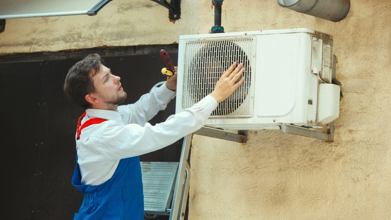 AC Repair Technician Inspecting Unit. Man in blue overalls checks the outdoor AC unit. Atlanta, GA property maintenance and HVAC services.