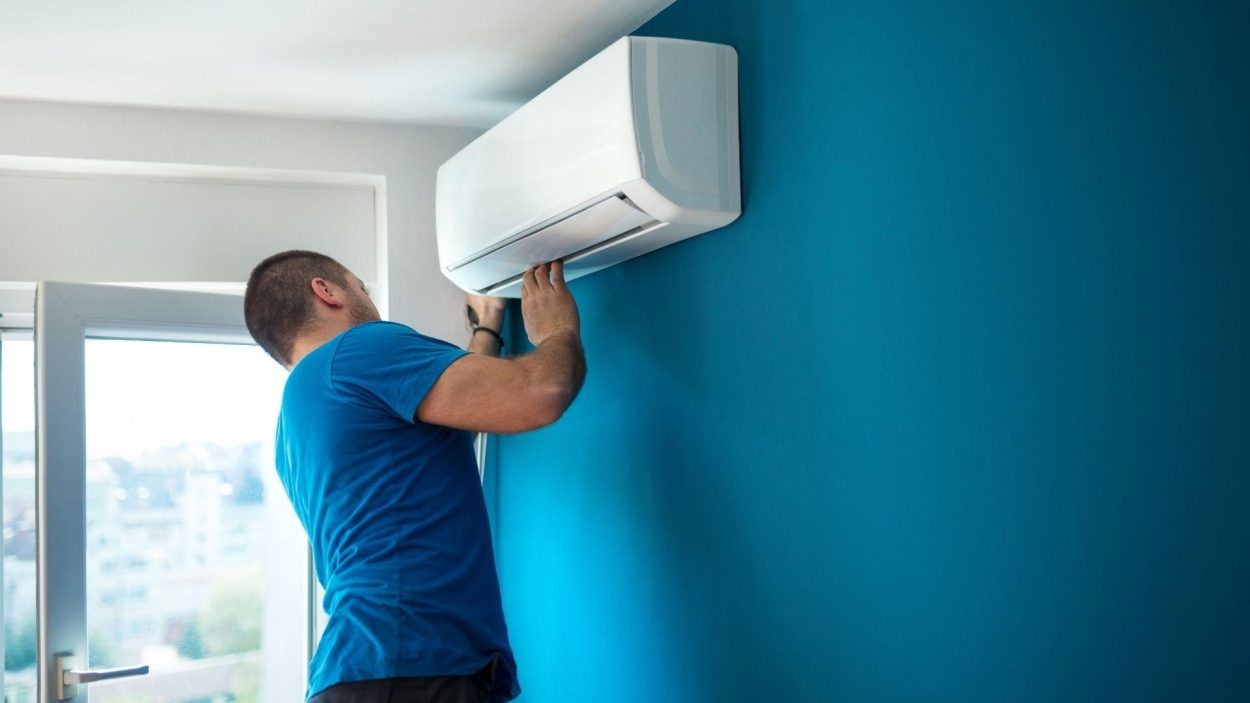 HVAC technician performing AC repair in Atlanta, GA. Man inspecting a wall-mounted air conditioning unit on a blue wall. Expert AC service.