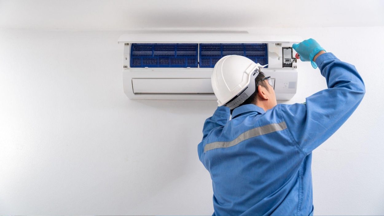 AC Repair Atlanta: Technician in blue uniform repairs a wall-mounted air conditioner for comfortable living in Atlanta, GA.