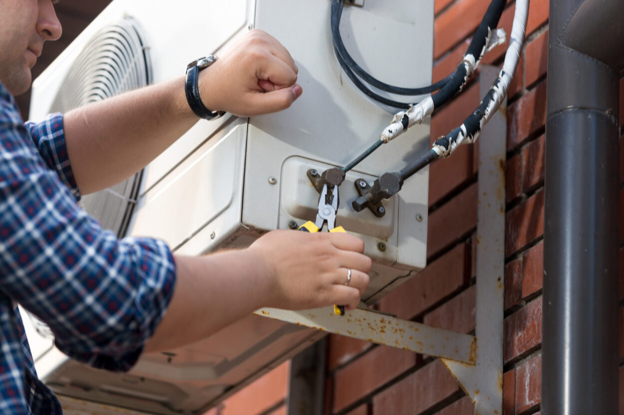 Male technician using pliers to repair outdoor air conditioning unit, emphasizing HVAC maintenance and repair services in Midtown Atlanta.
