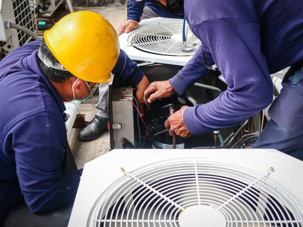 HVAC technicians in yellow hard hats repairing air conditioning unit, demonstrating expert HVAC service and maintenance in Decatur, GA.